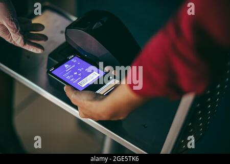 Eine nicht erkennbare Frau scannt beim Check-in am Flughafen ein Smartphone. Digitales Scannen auf der Bordkarte am Check-in-Schalter am Flughafen. Stockfoto