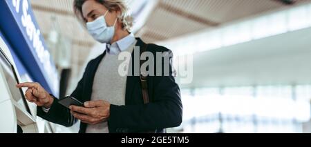 Männlicher Unternehmer, der den Check-in-Automaten am Flughafen nutzt. Ein Geschäftsmann ist auf Reisen und checkt am Flughafenterminal ein. Stockfoto