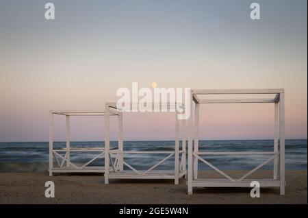 Drei hölzerne Pavillons am Meer bei Nacht mit Mond im Himmel Stockfoto