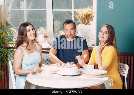 Mann und junge Frauen sitzen in der Wohnküche mit Kuchen auf dem Tisch und feiern Geburtstag. Stockfoto