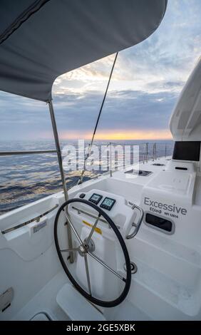 Lenkrad im Cockpit auf dem Deck eines Segel-Katamarans bei Sonnenuntergang, Segeltörn, Dodekanes, Griechenland Stockfoto