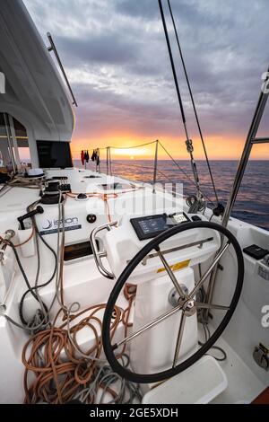 Lenkrad im Cockpit auf dem Deck eines Segel-Katamarans bei Sonnenuntergang, Segeltörn, Dodekanes, Griechenland Stockfoto