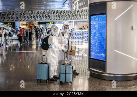 Doha, Katar. August 2021. Passagiere, die Gesichtsschutz, Masken und Schutzanzüge tragen, überprüfen auf dem internationalen Flughafen Hamad in Doha einen Bildschirm für das Einsteigen. Kredit: SOPA Images Limited/Alamy Live Nachrichten Stockfoto