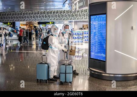 Doha, Katar. August 2021. Passagiere, die Gesichtsschutz, Masken und Schutzanzüge tragen, überprüfen auf dem internationalen Flughafen Hamad in Doha einen Bildschirm für das Einsteigen. (Bild: © Ivan Abreu/SOPA Images via ZUMA Press Wire) Stockfoto