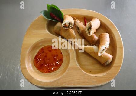 Blick aus der Perspektive auf frittierte Frühlingsrollen, serviert in Holztablett mit Dipping-Sauce. Stockfoto