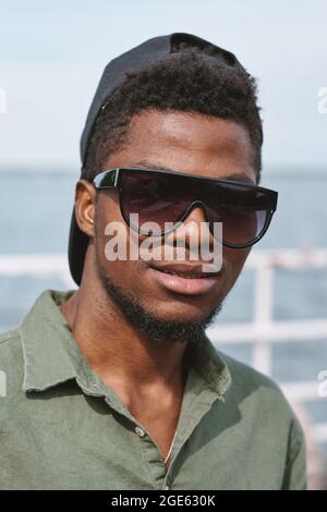 Das Gesicht eines hübschen, seriös aussehenden jungen Mannes mit Sonnenbrille und Mütze, der die Kamera anschaut Stockfoto