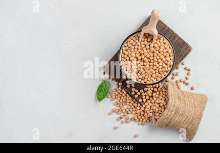 Rohe, getrocknete Kichererbsen in einer Schüssel und einem Beutel auf grauem Hintergrund. Stockfoto
