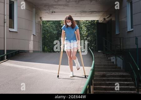 Eine Frau mit gebrochenem Bein geht mit orthopädischen Krücken eine Rampe hinunter. Stockfoto