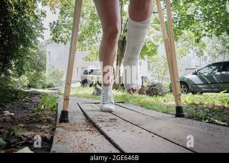 Eine Frau mit gebrochenem Bein geht mit orthopädischen Krücken eine Rampe hinunter. Stockfoto