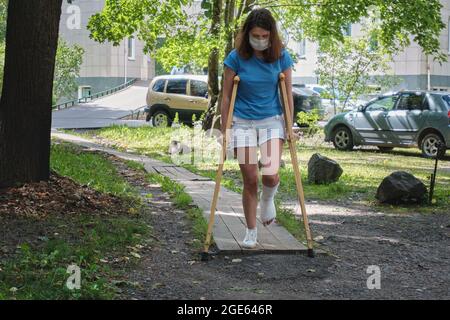 Eine Frau mit gebrochenem Bein geht mit orthopädischen Krücken eine Rampe hinunter. Stockfoto