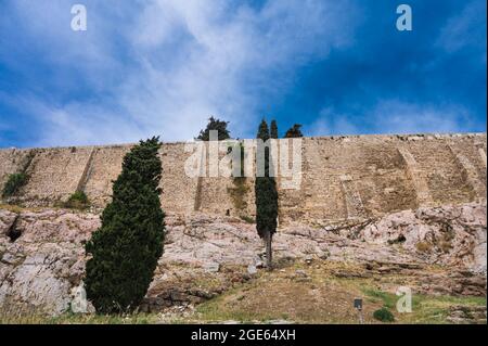 Blick von unten auf die Akropolis von Athen. Alte griechische Siedlung. Wahrzeichen von Athen. Grüne Bäume in der Nähe einer hohen Steinmauer. Stockfoto