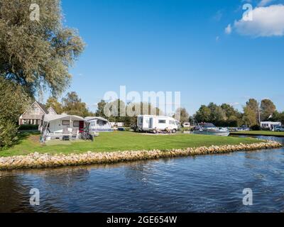 Menschen entspannen sich in der Nähe von Reisemobilen auf dem Campingplatz in Earnewald, Naturschutzgebiet Alde Feanen, Friesland, Niederlande Stockfoto