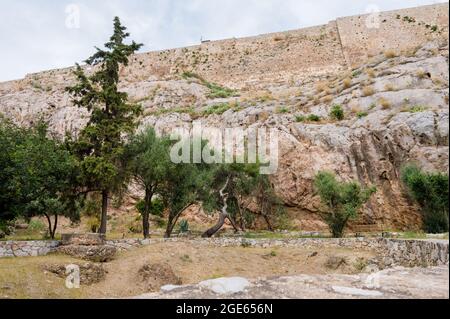 Blick von unten auf die Akropolis von Athen. Alte griechische Siedlung. Wahrzeichen von Athen. Grüne Bäume in der Nähe einer hohen Steinmauer. Stockfoto