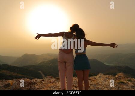 Zwei glückliche Freunde, die beim Sonnenuntergang im Berg die Arme ausstrecken Stockfoto