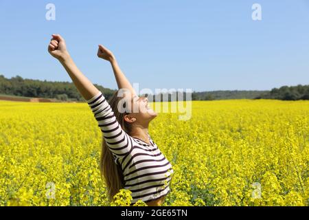 Eine aufgeregte Frau, die in einem gelben Feld die Arme hebt und den Frühling an einem sonnigen Tag feiert Stockfoto