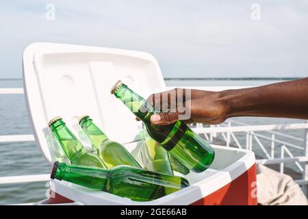 Hand eines Mannes, der eine Glasflasche mit kaltem, leckerem Bier aus der Kühlbox nahm, als er an einer Party am Pier teilnahm Stockfoto