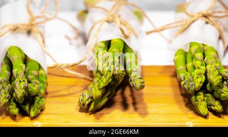 Frischer grüner Spargel auf Holztisch auf weißem Hintergrund. Gesunde pflanzliche Ernährung. Vegetarismus. Gemüsetapete. Stockfoto