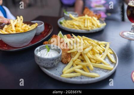 Mittagessen mit Fisch in Semmelbröseln und Teig, pommes Frites, Kartoffeln, Tartarsauce für Fisch. Pommes Frites und Thymian. Unscharfer Hintergrund im Freien. Stockfoto
