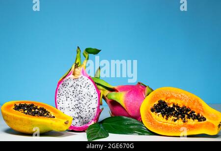 Hälften aus frischem Bio-Drachenfrucht und Papaya auf blauem Hintergrund, kreatives Sommer-Food-Konzept, Bannerhintergrund mit Kopierraum, Minimalismus Stockfoto