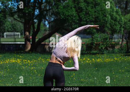 Die junge kaukasische blonde Frau in Sportkleidung macht im Park Yoga. Workout im Freien. Yoga-Posen Stockfoto