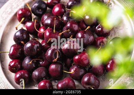 Haufen reifer Süsskirschen mit Stielen in einem Tablett. Rote Bio-Beeren auf einem Holztisch Stockfoto