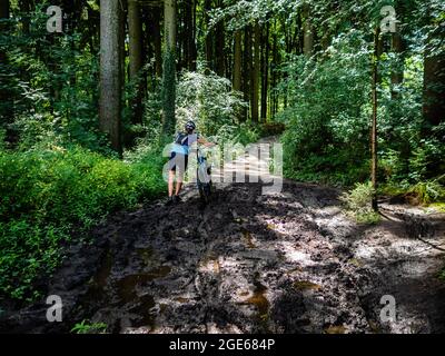 Eine Frau versucht mit ihrem Fahrrad einen schlammigen Weg zu gehen.Anlässlich der zehnten Ausgabe des Niederländischen Bergfilmfestivals und in voller Tradition des Jubiläumsweges in den Alpen wurde 2020 eine neue Wanderroute, der Niederländische Bergweg, eingerichtet. Diese Route ist eine zerklüftete Wanderung von über 100 km, die die sieben steilsten Berggipfel in Süd-Limburg verbindet. Die Route beginnt am Wilhelminaberg in Landgraaf und endet am Observant in Maastricht. Sie ist nicht die längste, aber sie ist die härteste Strecke des Landes geworden, die an einigen Stellen die deutsche und belgische Grenze überquert. Stockfoto