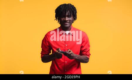 KIEW, UKRAINE - 01. AUGUST 2021: Glücklicher afroamerikanischer Mann spielt Videospiel isoliert auf Gelb Stockfoto