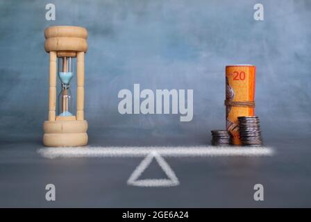Balance zwischen Zeit- und Geldkonzept. Sandglas, Banknoten und Stapel-Münzen auf Waage Stockfoto