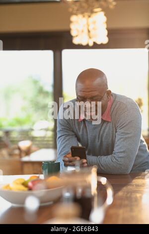 Glücklicher älterer afroamerikanischer Mann, der in der modernen Küche steht und Smartphone benutzt Stockfoto