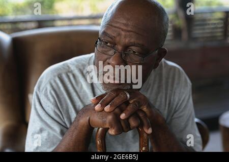 Nachdenklicher älterer afroamerikanischer Mann, der auf dem Spazierstock sitzt und sich lehnt Stockfoto