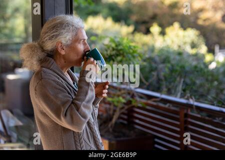 Entspannende ältere kaukasische Frau auf dem Balkon, die Kaffee trinkt Stockfoto