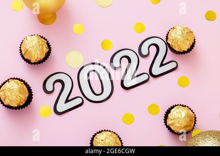 2022 Text mit Weihnachtsschmuck Süßigkeiten Bonbons Goldkonfetti auf rosa Hintergrund. Tores 2022 Schriftzug im Happy New Year Stil. Stockfoto