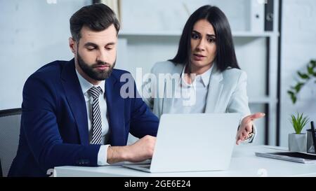 Trauriger Geschäftsmann hört Geschäftsfrau streitend und zeigt auf Laptop Stockfoto