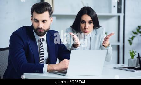 Trauriger Geschäftsmann schaut weg, während Geschäftsfrau streitig und zeigt auf Laptop Stockfoto