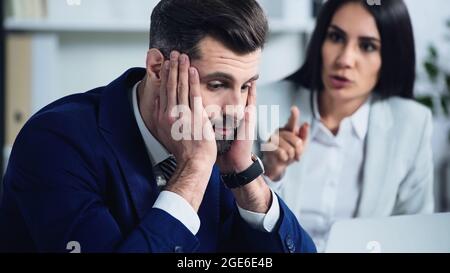 Trauriger Geschäftsmann berührt Gesicht in der Nähe verschwommene Geschäftsfrau streitig im Büro Stockfoto
