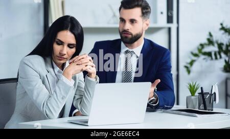 Traurige Geschäftsfrau, die in der Nähe von verschwommenen Geschäftsleuten, die im Büro streiten, wegschaut Stockfoto