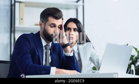 Trauriger Geschäftsmann, der in die Nähe verschwommener unzufriedener Geschäftsfrau schaut, die im Büro streitig ist Stockfoto
