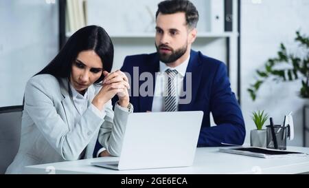 Verärgerte Geschäftsfrau, die in die Nähe verschwommener Geschäftsmänner schaut, die sich im Büro streiten Stockfoto