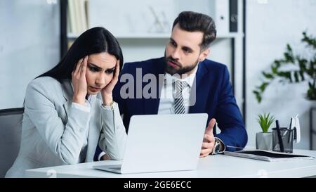 Verärgerte Geschäftsfrau berührt Kopf in der Nähe verschwommenen Geschäftsmann Streit im Büro Stockfoto