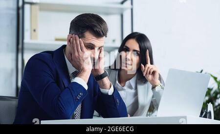 Trauriger Geschäftsmann, der in der Nähe einer verschwommenen Geschäftsfrau mit dem Finger zeigt, während er im Büro streitete Stockfoto