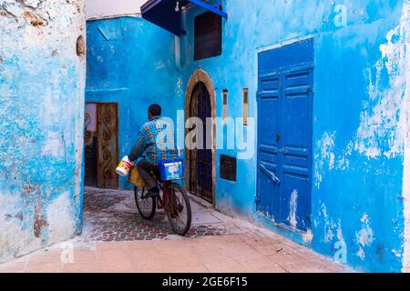 Marokko, Essaouira: Jemand, der mit dem Fahrrad in einer Straße der Medina mit blau gestrichenen Wänden fährt, die Medina ist als UNESCO-Weltkulturerbe registriert Stockfoto