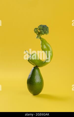 Frisches grünes Gemüse Food Balance auf gelbem Hintergrund, Avocado, Pfeffer und Brokkoli vegetarische und vegane Ernährung balancieren kreative Lebensmittelkonzept, Kopie Stockfoto