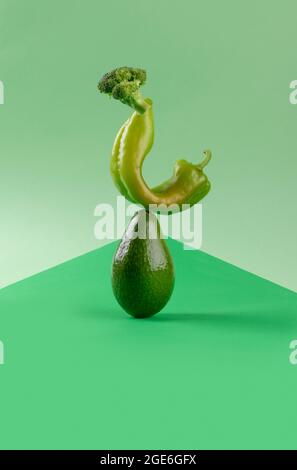 Frisches grünes Gemüse Food Balance auf grünem geometrischen Papier Hintergrund, Avocado, Pfeffer und Brokkoli vegetarische und vegane Ernährung balancieren kreative foo Stockfoto