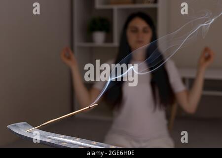 Ein aromatischer Indianerstab brennt, die Frau im Hintergrund meditiert. Aromatherapie, Selbsteintauchen, die Kraft des Denkens Stockfoto