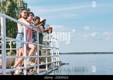 Eine bunte Gruppe von glücklichen Freunden, die am Pier stehen und das Wasser betrachten Stockfoto