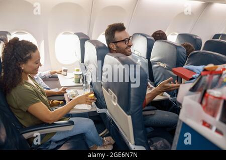 Fröhliche Passagiere lächeln und warten auf eine weibliche Flugbegleiterin, die das Mittagessen an Bord serviert Stockfoto