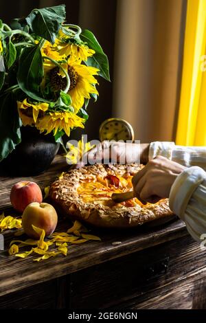 Galette mit Pfirsichen. Ein Teil der Galette und Sonnenblumen im Fokus Stockfoto