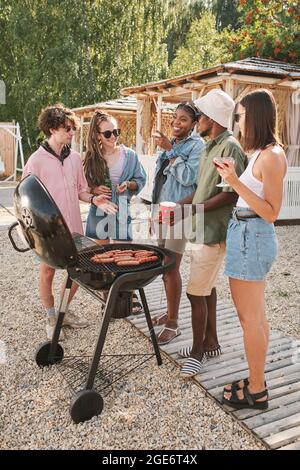 Hübsche junge Frau, die ihren Freunden auf der Strandparty einen Witz erzählt, wenn sie Hot Dogs und Getränke trinken Stockfoto