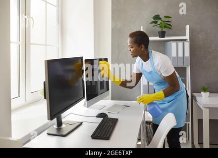 Glückliche Frau vom Reinigungsservice, der Computerbildschirme im modernen Büro abwischt Stockfoto