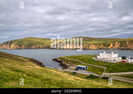 Alte Leuchtturm-Uferstation im Hermaness National Nature Reserve in Unst, Shetland. Mit alter Saxa Vord RAF Station im Hintergrund. Stockfoto